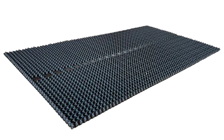 Dreneringselement i svart plast på svart bakgrunn: en tynn, rektangulær plate med tett mønster av små knotter/kupler på overflaten, vist i skrått perspektiv.