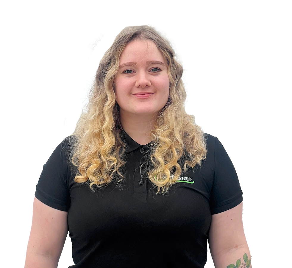 Isolert portrett av Mina Wold på gjennomsiktig bakgrunn: smilende kvinne med langt, bølgete blondt hår, runde solbriller med tonede glass og svart t-skjorte, med armene bak ryggen.