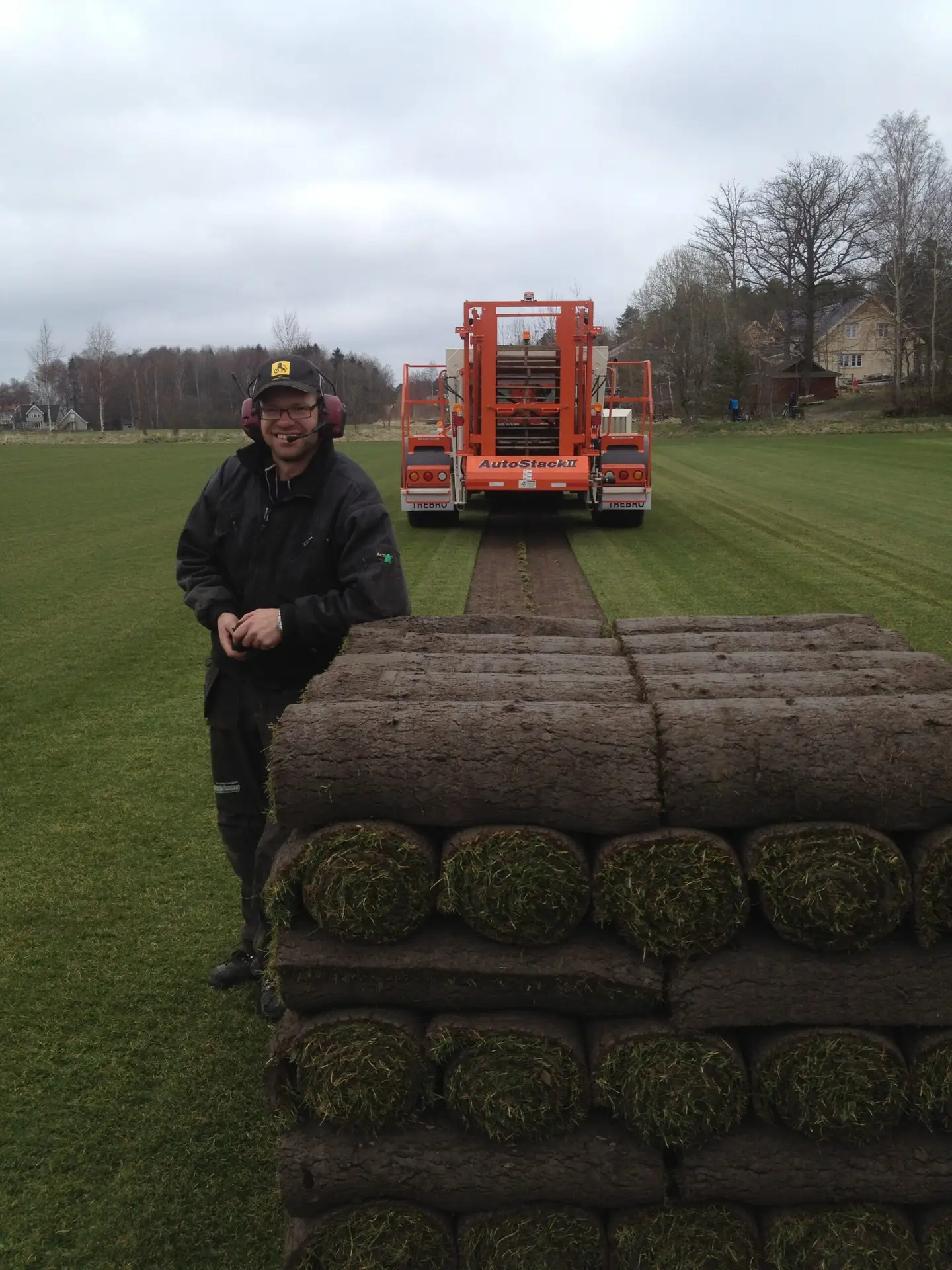 Ole Skaarnes ved ferdigplenruller på jordet, med høstemaskin i bakgrunnen.
